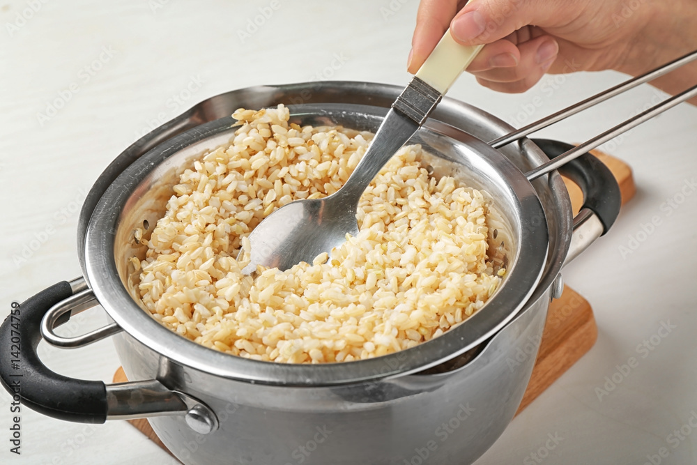 Hand with spoon stirring brown rice in colander on kitchen table