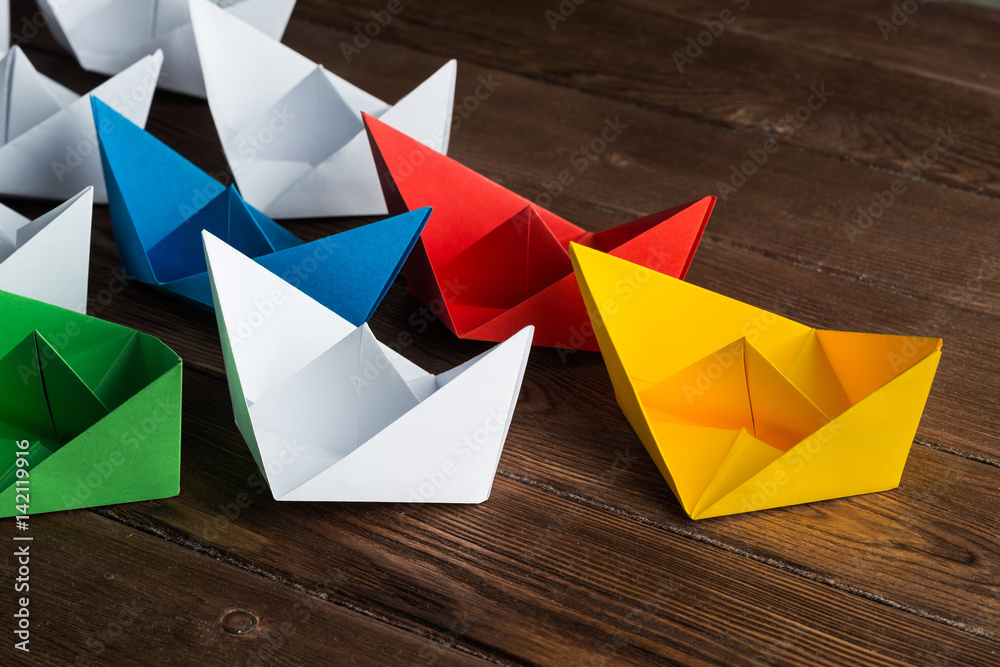 Business leadership concept with white and color paper boats on wooden table