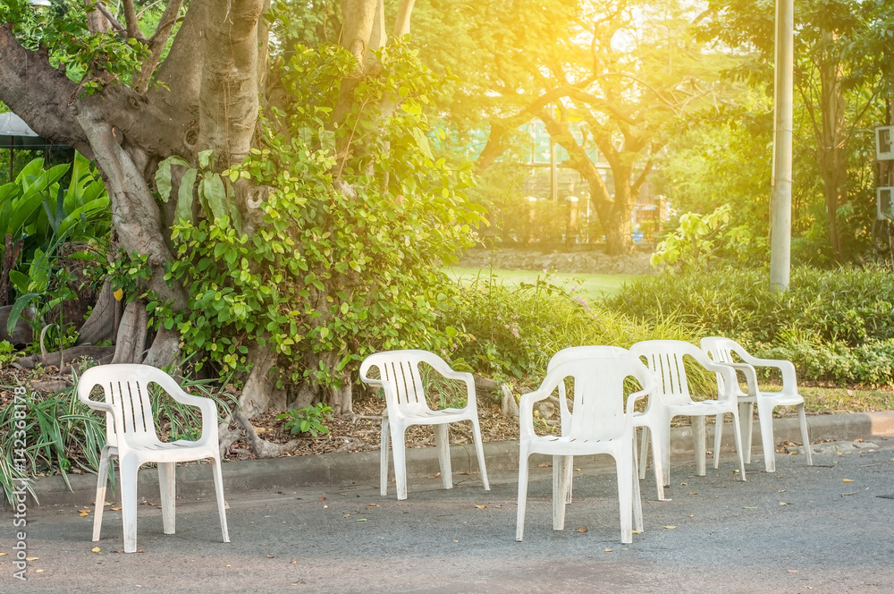 Group of white plastic chairs in green park with light flare.