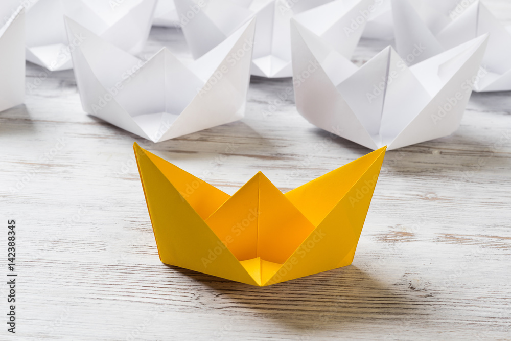 Business leadership concept with white and color paper boats on wooden table