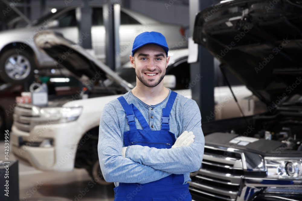 Young mechanic standing in front of open car hood