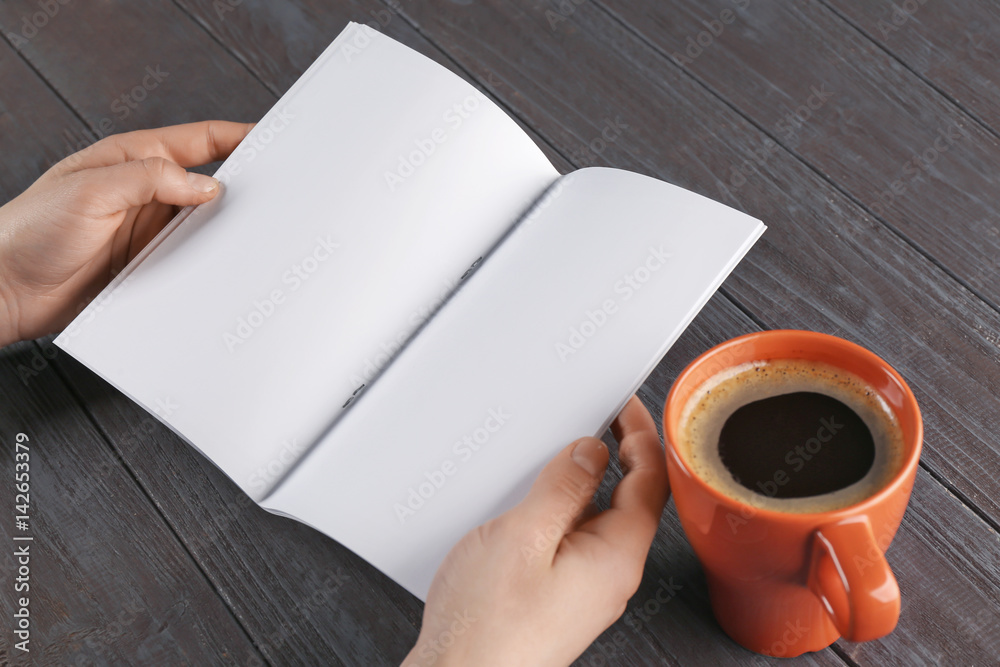 Female hands holding blank brochure on wooden background