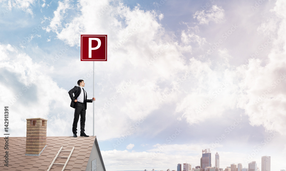 Young businessman with parking sign standing on brick roof. Mixed media