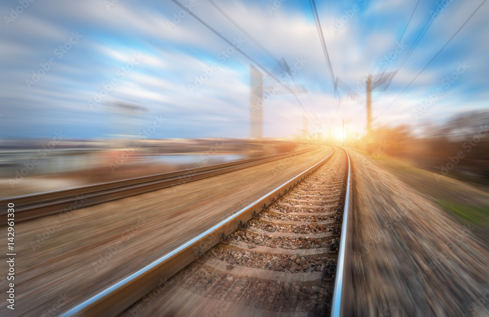 Railroad in motion at sunset. Railway station with motion blur effect and colorful sky with clouds. 