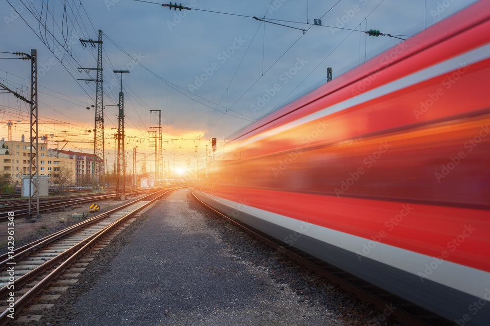 High speed red passenger train on railroad track in motion at sunset. Blurred commuter train on the 