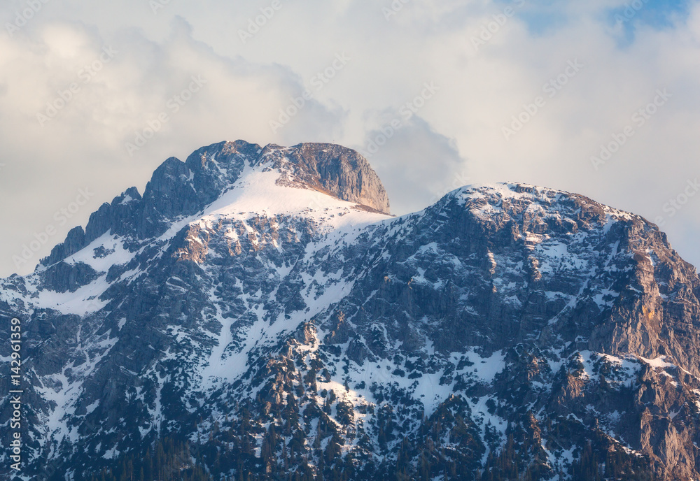 Snowy mountain peaks at sunset in spring. Mountain landscape with high rocks covered with snow, fore