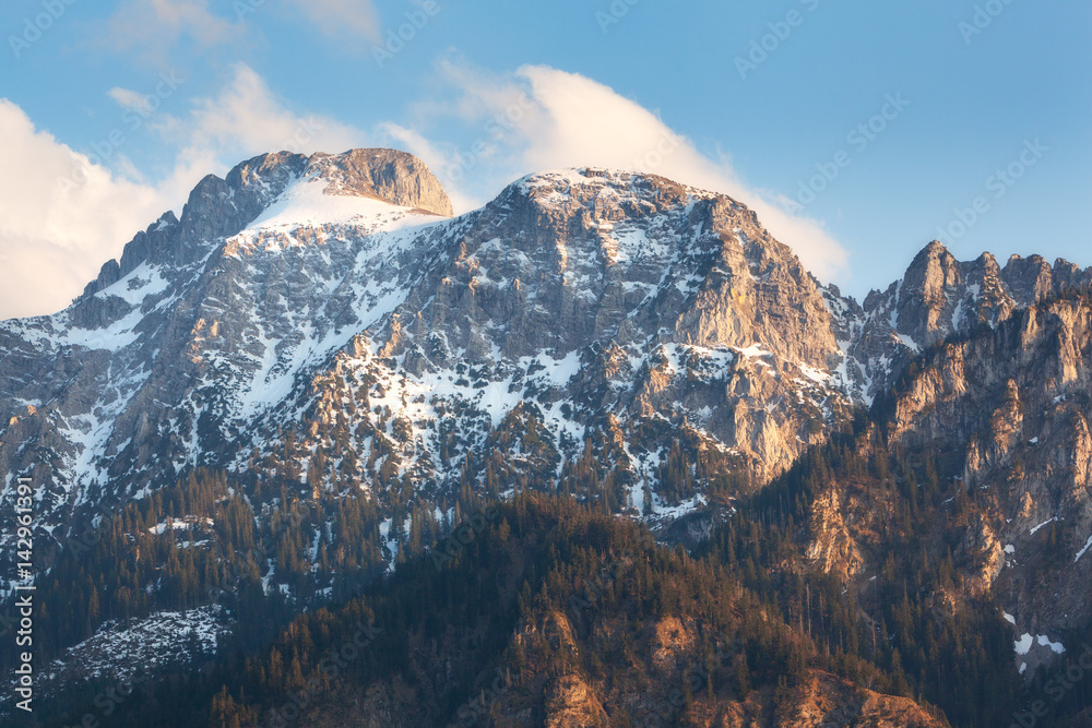 Snowy mountain peaks at sunset in spring. Mountain landscape with high rocks covered with snow, fore