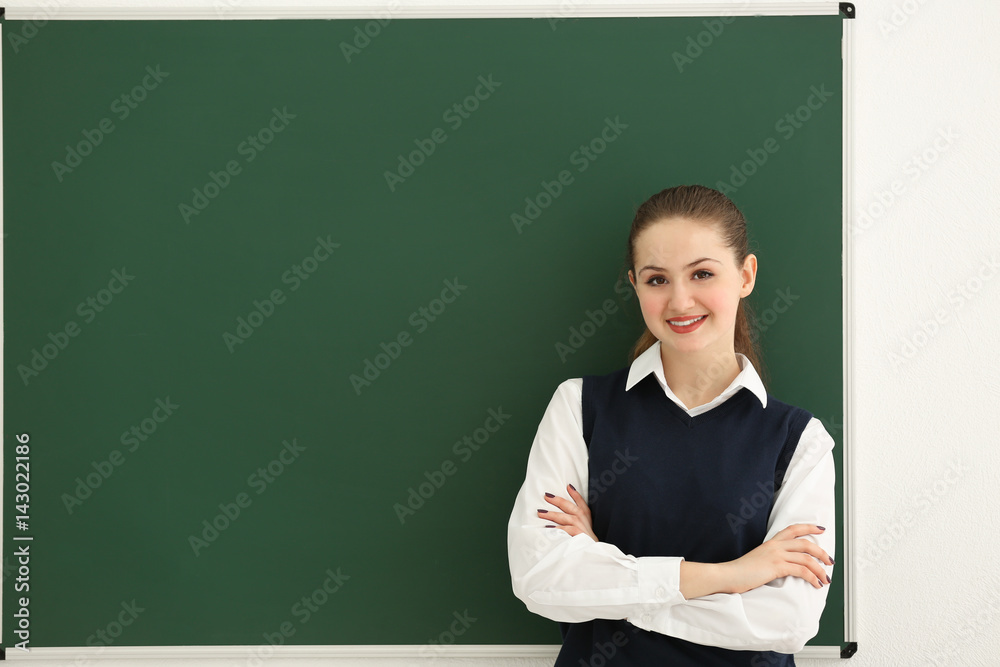 Smiling schoolgirl with crossed arms standing at blackboard in classroom