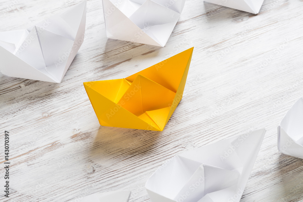 Business leadership concept with white and color paper boats on wooden table