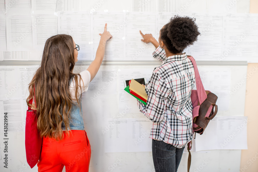 Female students looking at the lesson schedule at the university corridor