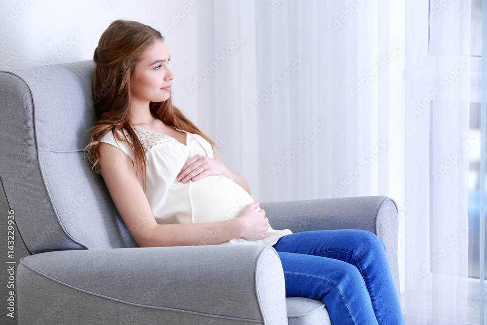 Beautiful pregnant woman sitting in armchair at home