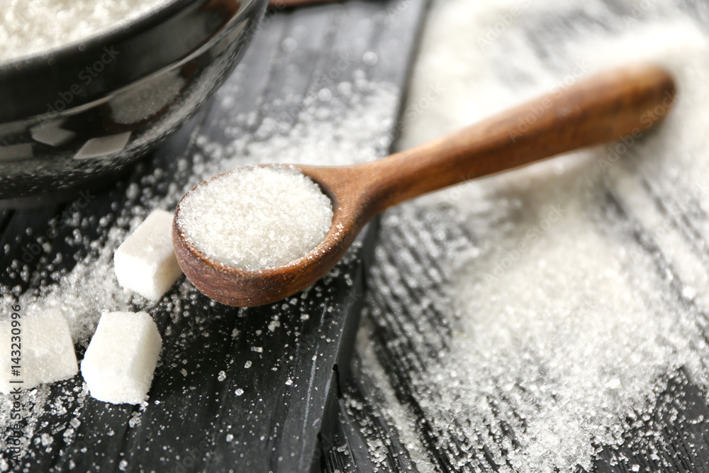 Wooden spoon with white granulated sugar on black wooden background