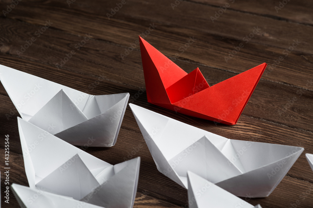 Business leadership concept with white and color paper boats on wooden table