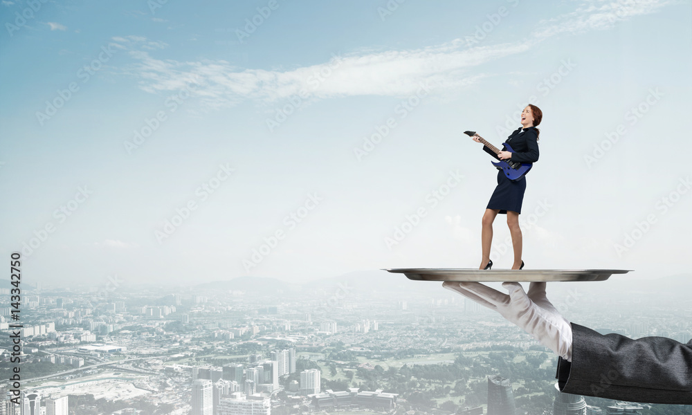 Attractive businesswoman on metal tray playing electric guitar against cityscape background