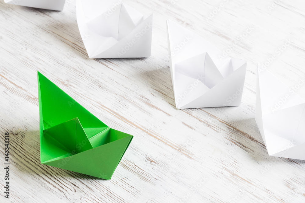 Business leadership concept with white and color paper boats on wooden table