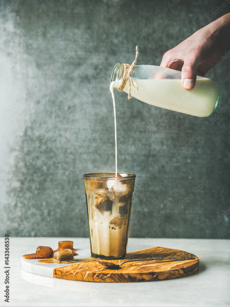 Mans hand pour milk from bottle to Iced焦糖拿铁咖啡鸡尾酒with冰冻咖啡冰块