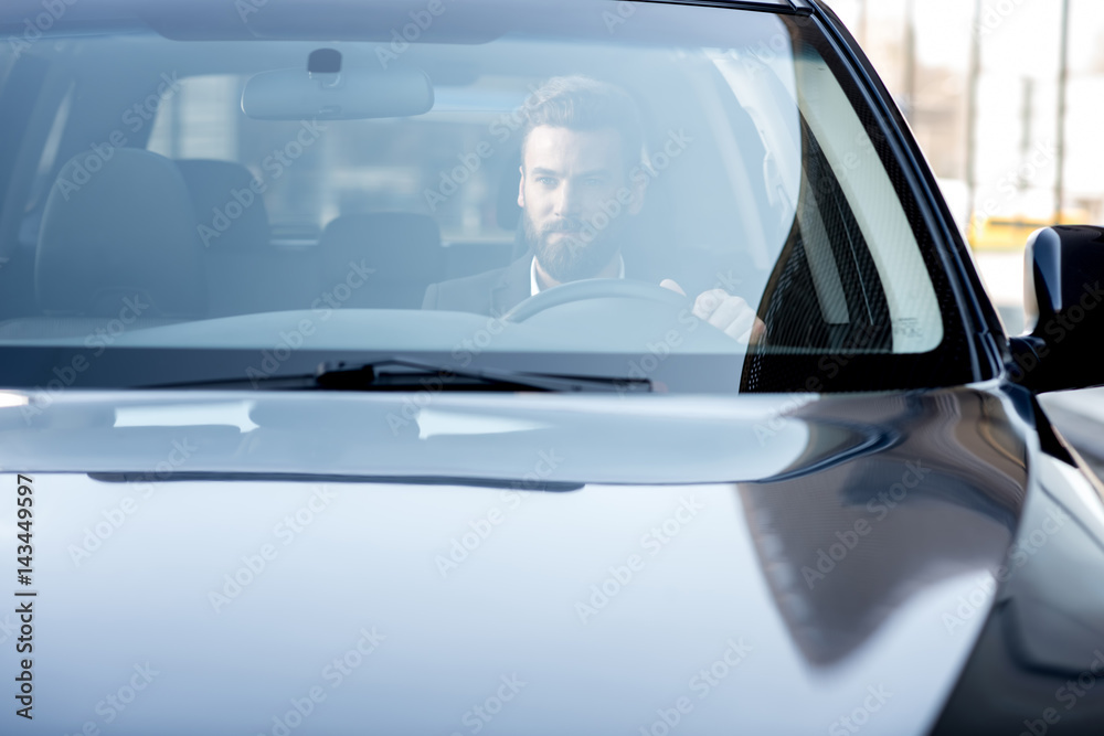 Handsome businessman driving a car in the city. View through the windshield with reflection and copy