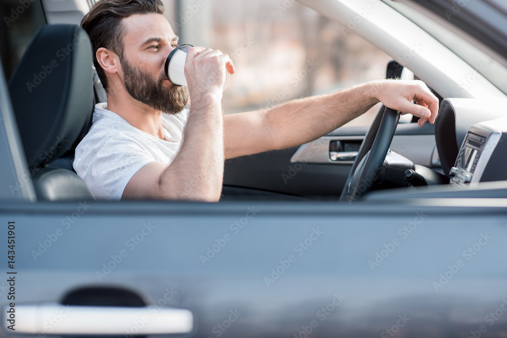 Handsome man dressed cassual in white t-shirt driving a car with coffee to go