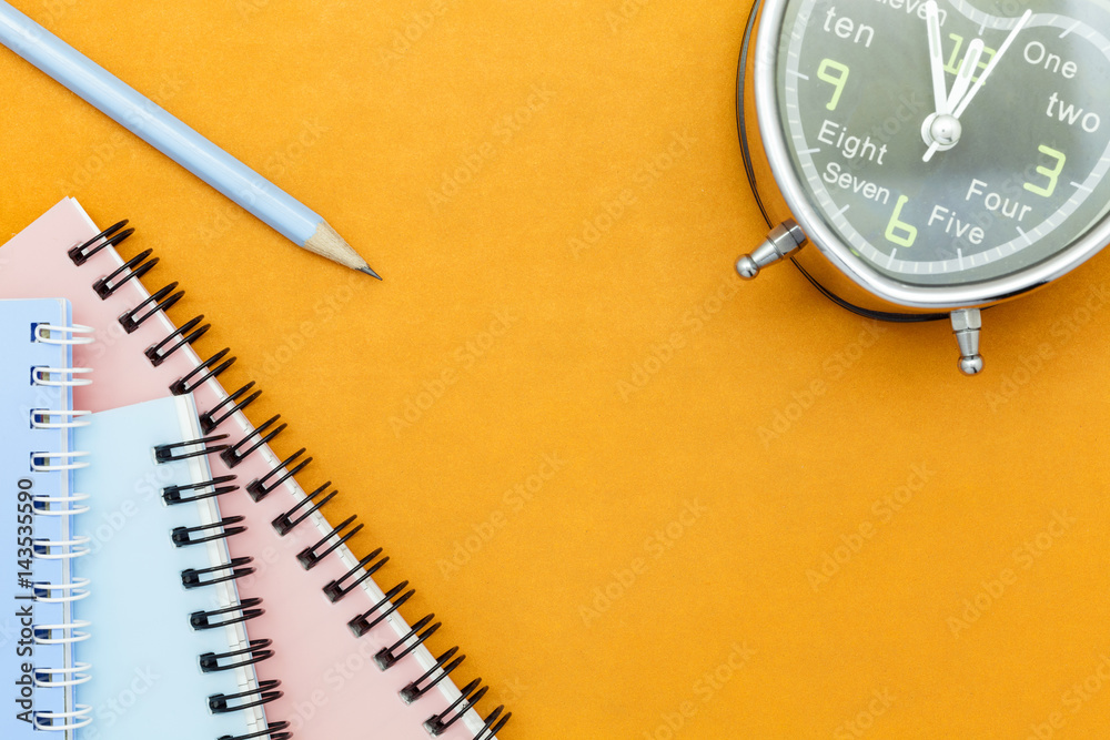 pencil with notebook and alarm clock on orange paper background.