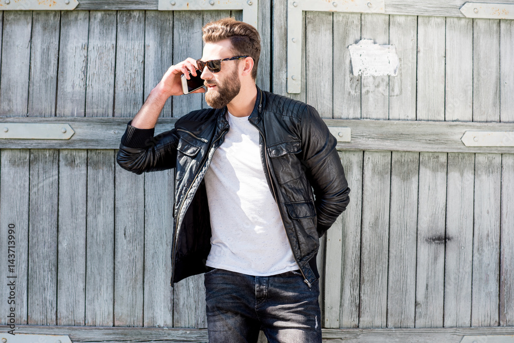 Portrait of a handsome man dressed in white t-shirt, jacket and jeans with phone on the old wooden b