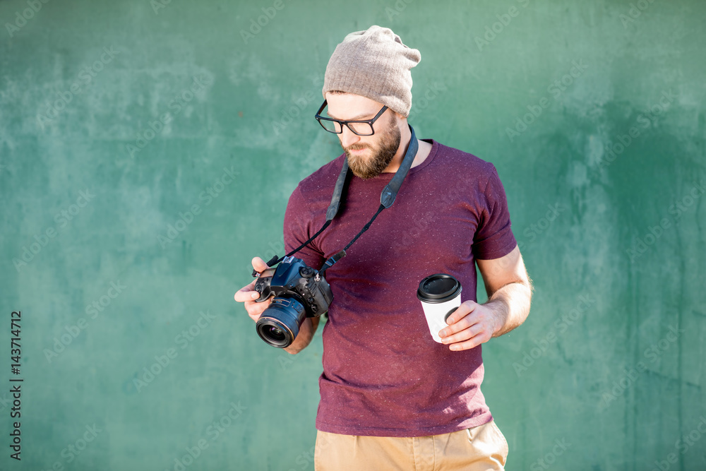 Portrait of a stylish photographer dressed casual in t-shirt and hat standing with camera on the gre