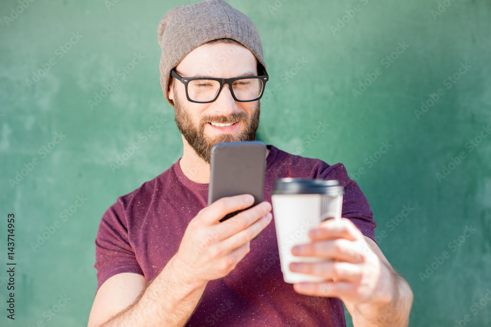 Stylish man photographing with phone coffee cup standing on the green background