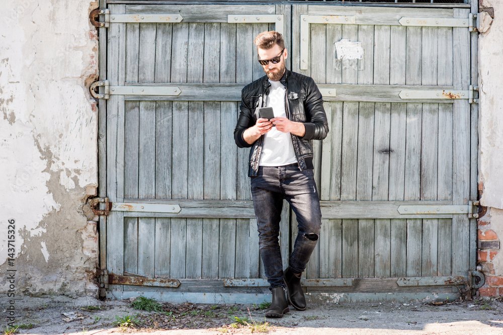 Portrait of a handsome man dressed in white t-shirt, jacket and jeans with phone on the old wooden b