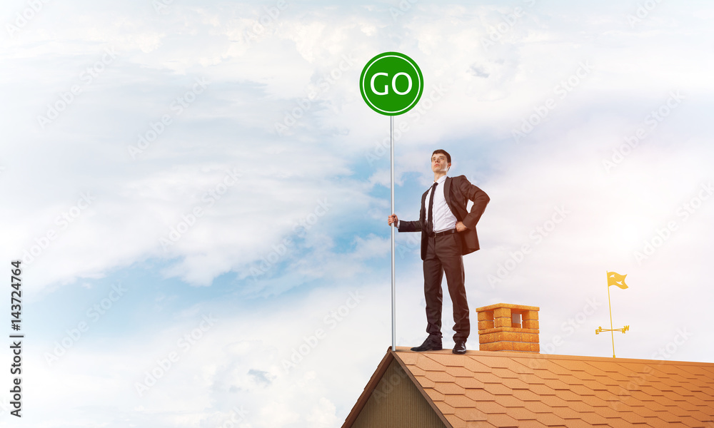 Businessman in suit on house top with ecology concept signboard. Mixed media