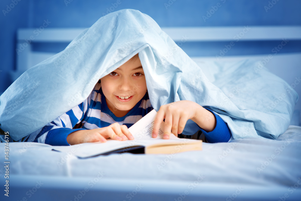 boy lying in bed with a book. child reading