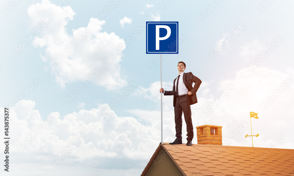 Young businessman with parking sign standing on brick roof. Mixed media