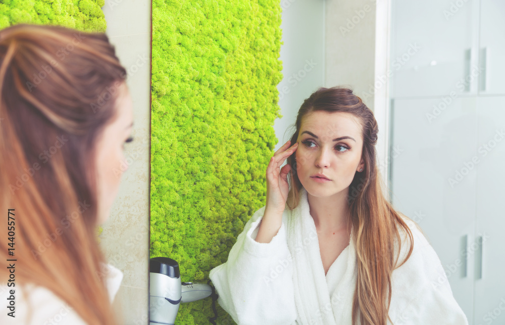 Pretty woman looking at mirror in modern bathroom and checking wrinkles