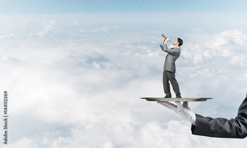 Businessman on metal tray playing fife against blue sky background