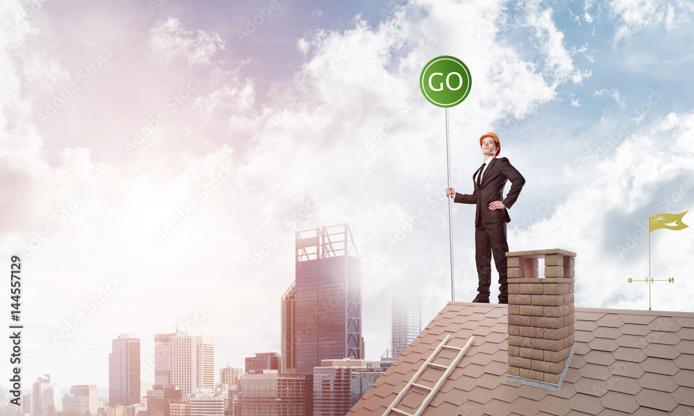 Businessman in suit on house top with ecology concept signboard. Mixed media