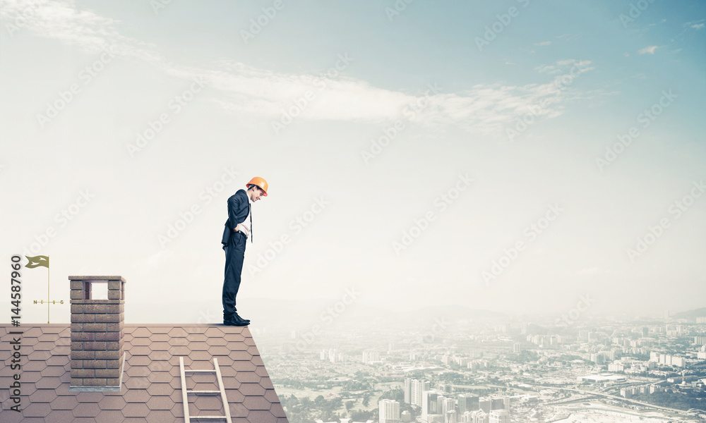 Businessman looking down from roof and modern cityscape at backg