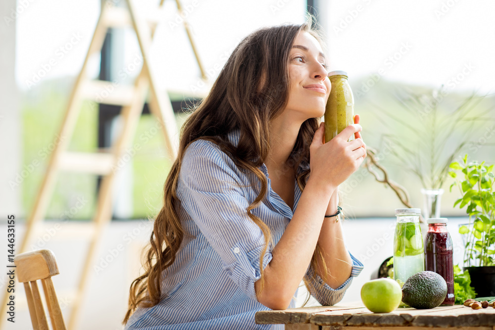 Beautiful woman sitting with drinks and healthy green food at home. Vegan meal and detox concept