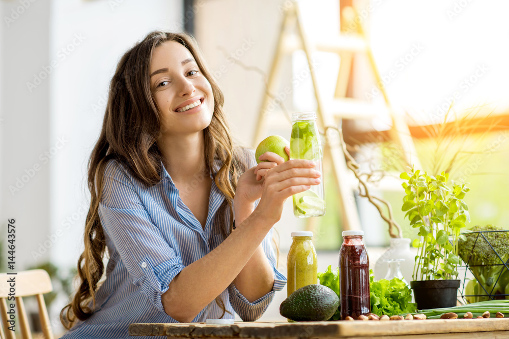 Beautiful happy woman sitting with drinks and healthy green food at home. Vegan meal and detox conce