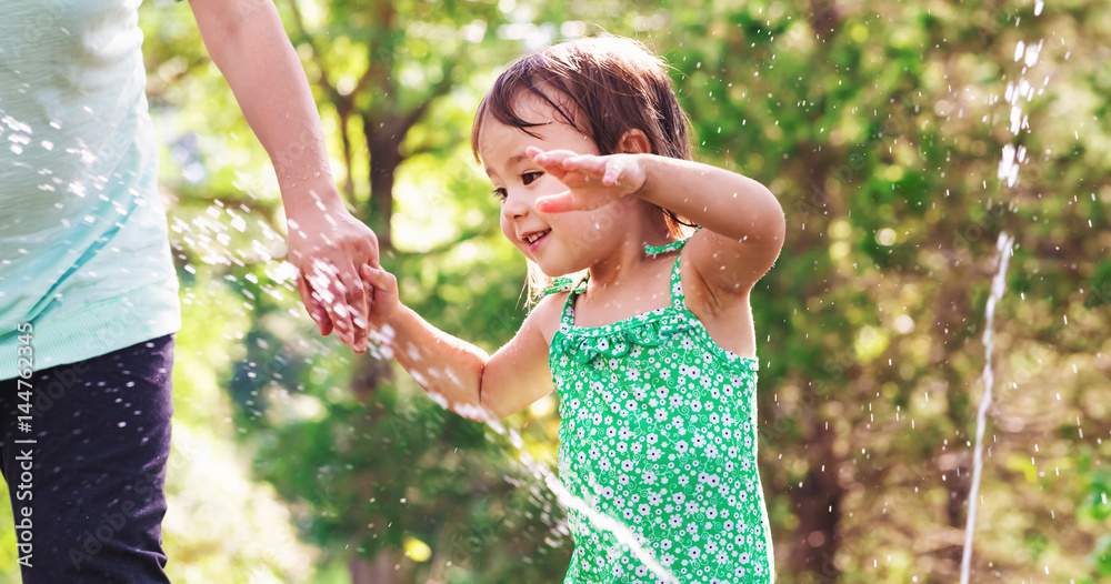 Toddler girl playing in a sprinkler with her mother