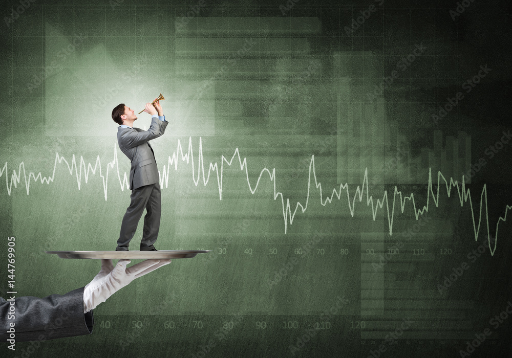 Young businessman on metal tray playing fife against concrete background with chart