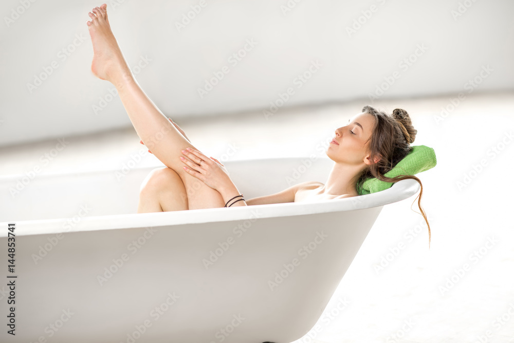 Beautiful young woman taking care about legs lying in the bathtube in the bathroom