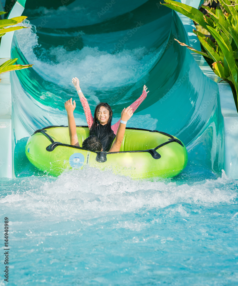 Asian child play water by slider down to the swimming pool