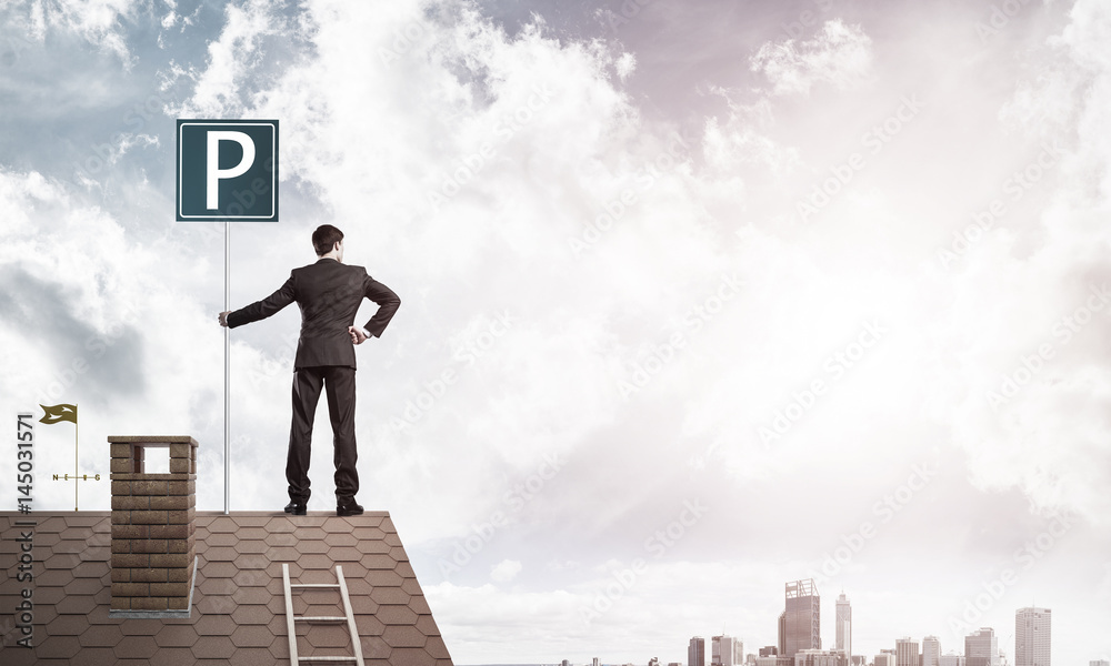 Young businessman with parking sign standing on brick roof. Mixe