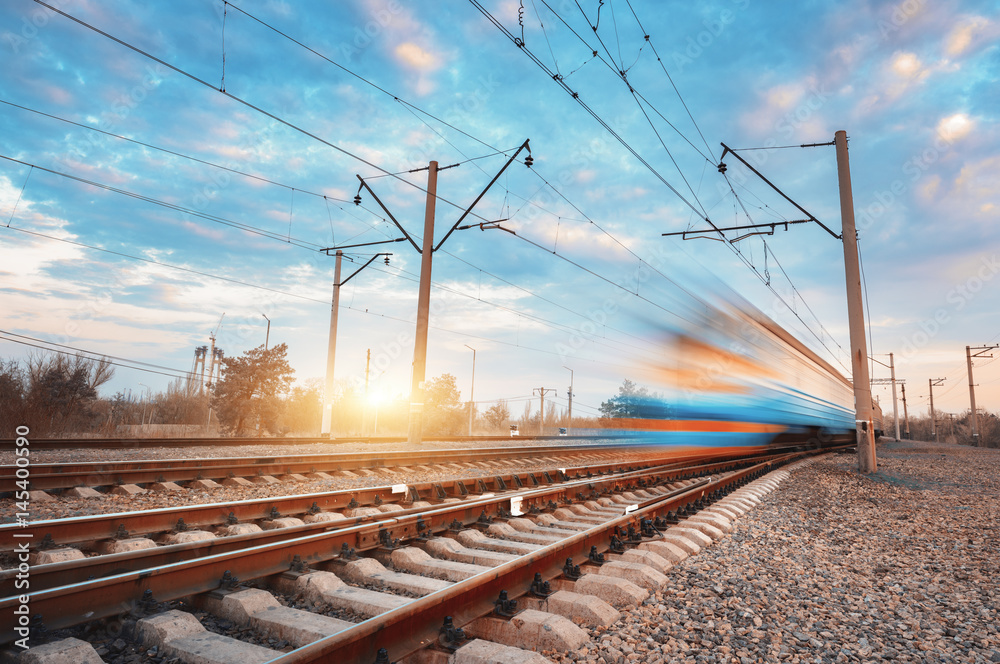 High speed blue passenger train in motion on railroad at sunset. Blurred commuter train. Railway sta