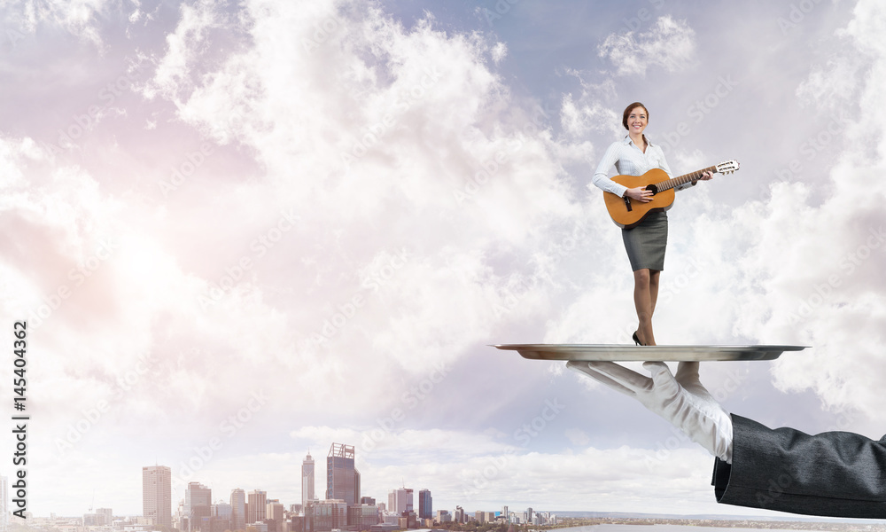 Attractive businesswoman on metal tray playing acoustic guitar against cityscape background