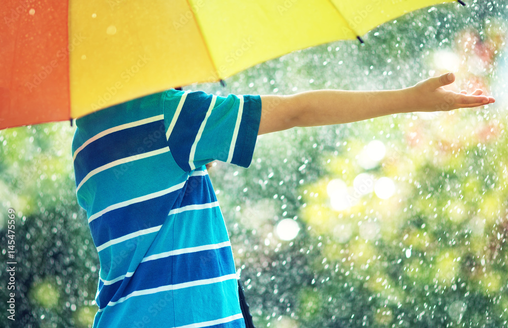 雨天的孩子。夏天的男孩在雨中撑着五颜六色的伞