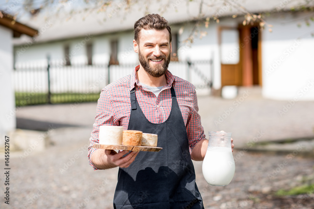 Portrait of a handsome farmer in apron walking with goat cheeses and milk outdoors on the rural hous