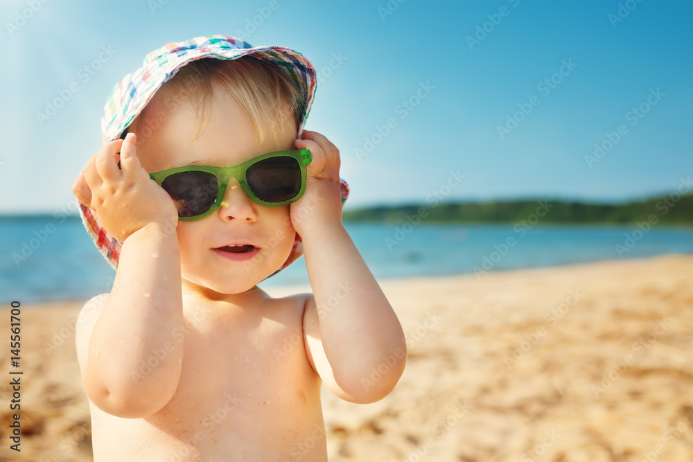 little boy smiling at the beach in hat with sunglasses