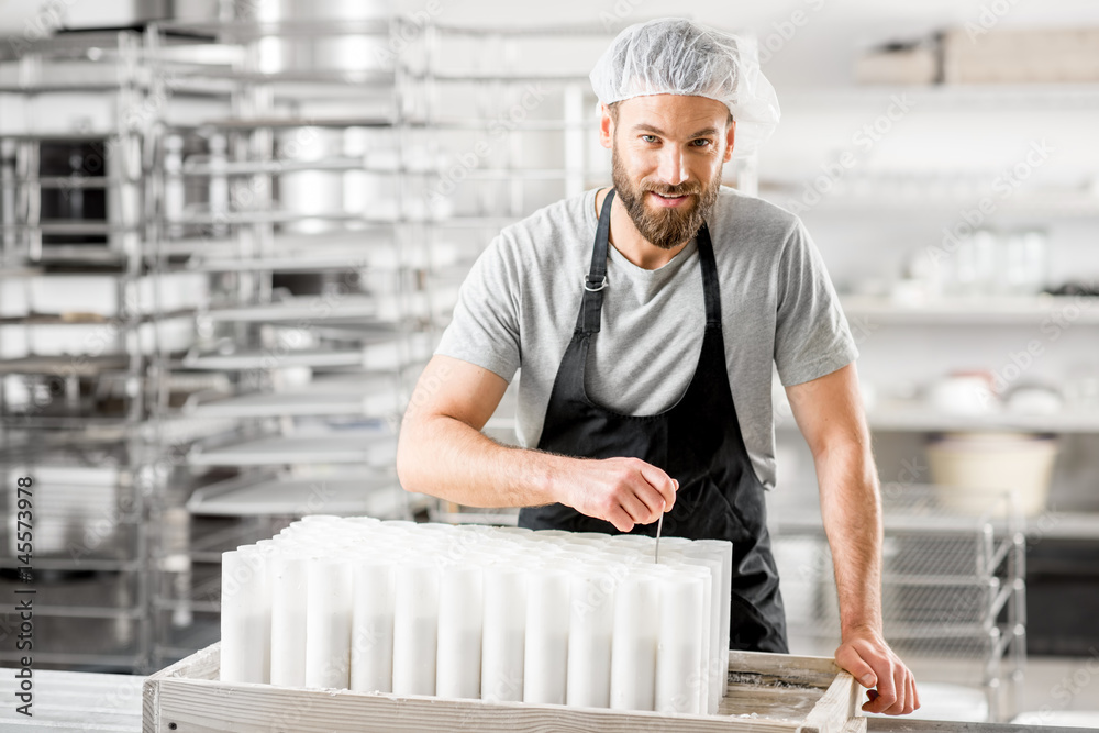 Portrait of a handsome cheese maker in uniform forming cheese into molds at the small producing farm