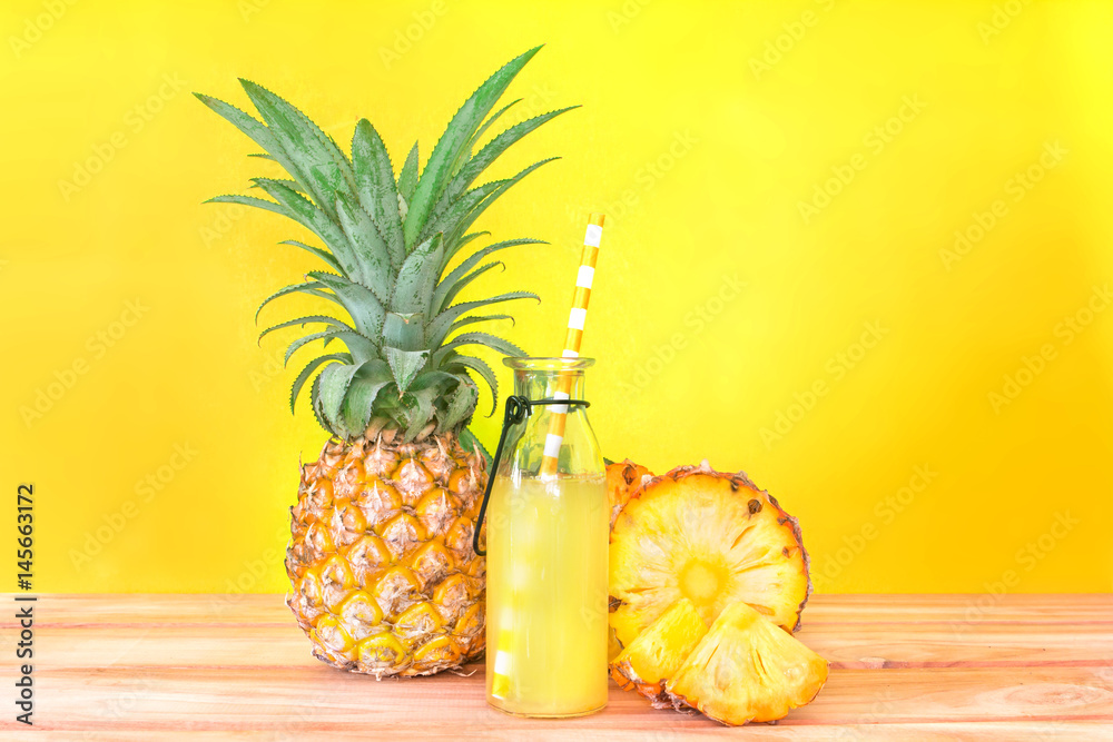 The Bottles of pineapple juice with sliced pineapple fruit on wooden table with vibrant yellow backg