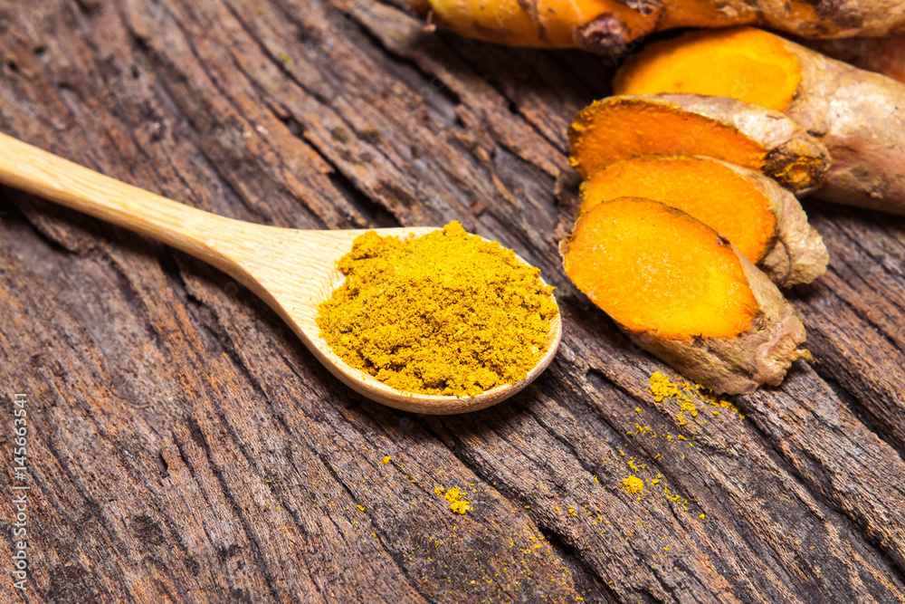 turmeric powder in spoon and roots on wooden plate