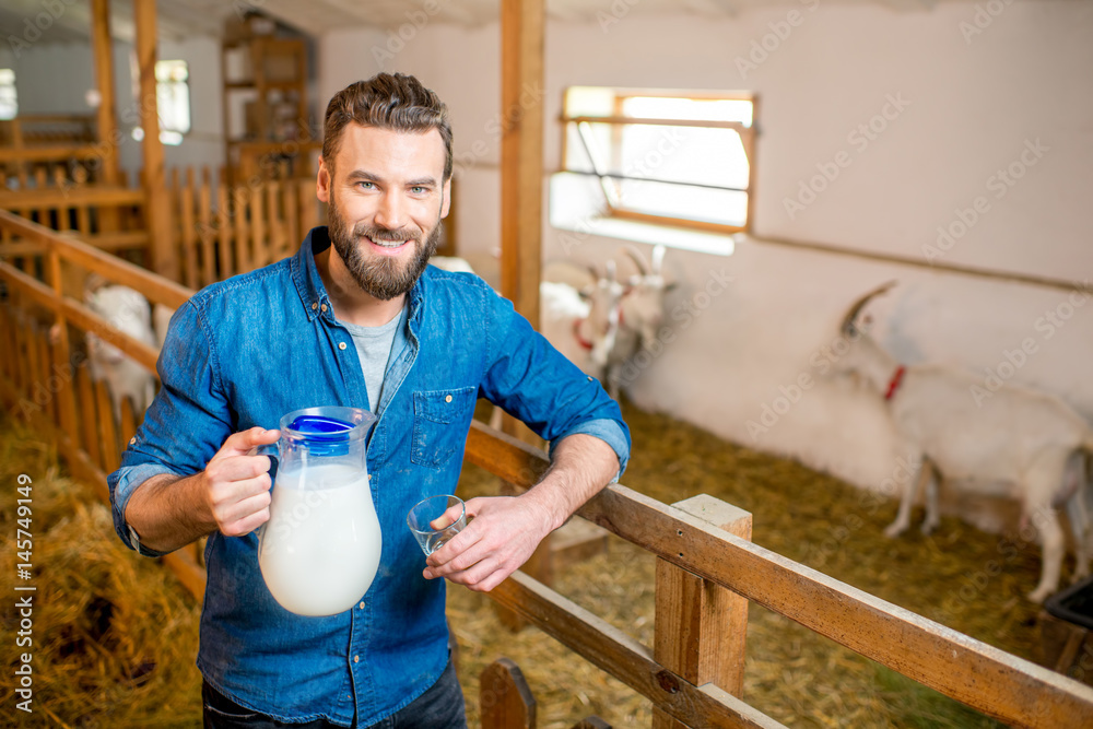 Portrait of a handsome farmer with fresh milk standing in the goat barn with goats on the background